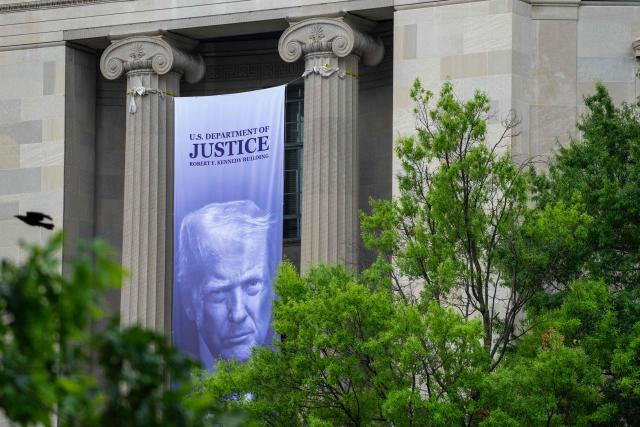 A banner featuring US President Donald Trump hangs on the outside of the Department of Justice headquarters ahead of a press conference with Acting Attorney General Todd Blanche announcing annual healthcare fraud takedown results in Washington, DC on June 23, 2026. (Photo by Ken Cedeno / AFP)