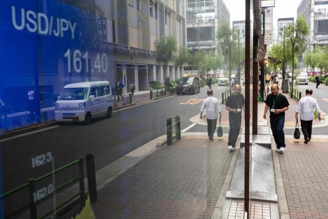 People are seen on a street as they pass a US dollar currency conversion board in Tokyo on June 23, 2026. The Tokyo stock market took a beating, shedding 3.6 percent, with investors keeping an eye on the yen as it came close to a 40-year low against the dollar, making exports including oil more expensive for Japan. (Photo by ANDREW CABALLERO-REYNOLDS / AFP)