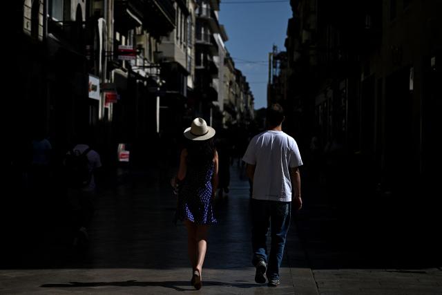 A man and a woman wearing a hat to shelter from the sun walk down a street in Bordeaux, southwestern France on June 23, 2026, as France experiences a heatwave. (Photo by Christophe ARCHAMBAULT / AFP)