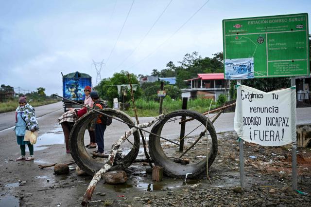 Indigenous people wait for transportation at the site where a road blockade had taken place, with a sign reading "We demand the resignation of Rodrigo Paz. Out!," on the highway connecting Cochabamba and Santa Cruz, in Cochabamba, Bolivia, on June 23, 2026. Former Bolivian President Evo Morales announced on June 22, 2026 the lifting of the roadblocks that remained in the department of Cochabamba, after Rodrigo Pazs government had declared a state of emergency three days earlier to put an end to the protests across the country. (Photo by MARTIN BERNETTI / AFP)