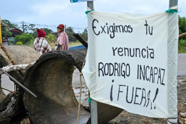 Indigenous women wait for transportation at the site where a road blockade had taken place, with a sign reading "We demand the resignation of Rodrigo Paz. Out!," on the highway connecting Cochabamba and Santa Cruz, in Cochabamba, Bolivia, on June 23, 2026. Former Bolivian President Evo Morales announced on June 22, 2026 the lifting of the roadblocks that remained in the department of Cochabamba, after Rodrigo Pazs government had declared a state of emergency three days earlier to put an end to the protests across the country. (Photo by MARTIN BERNETTI / AFP)