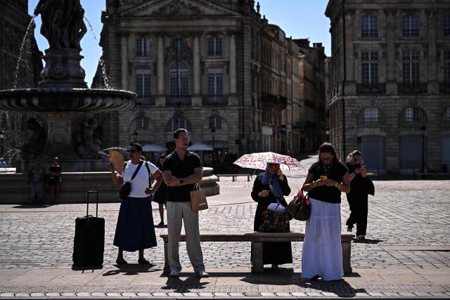 Commuters use a hand fan and an umbrella to cool down as they wait for a tramway in Bordeaux, southwestern France on June 23, 2026, as France experiences a heatwave. (Photo by Christophe ARCHAMBAULT / AFP)