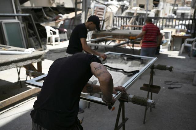 An aluminium worker supporting a tattoo that reads 'Mohammad' referring to Islam's Prophet Mohammad, repairs a door belonging to homes and businesses damaged during the earlier Israeli military strikes on the southern Lebanese coastal city of Tyre on June 23, 2026. On June 22, 2026, mediators Pakistan and Qatar said that Tehran and Washington had agreed to set up a "de-confliction cell" to limit flare-ups in Lebanon following talks in Switzerland on ending the wider Middle East war, which Tehran has linked to halting the parallel conflict in Lebanon. (Photo by Joseph EID / AFP) / 