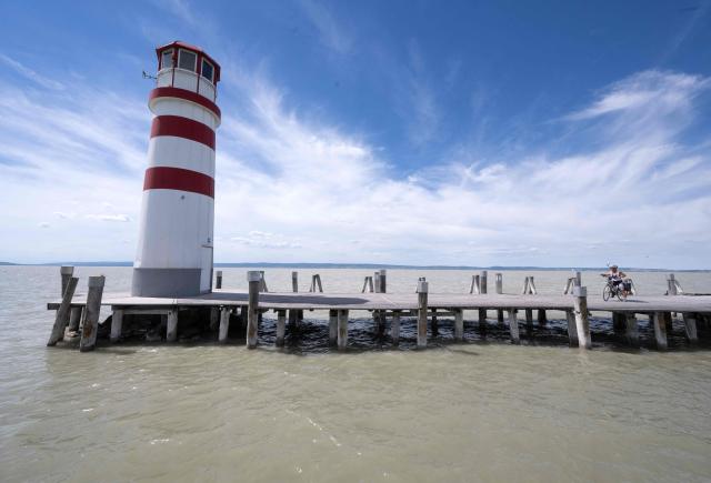 A woman rests on her bicycle along the lighthouse at Neusiedl See lake at Podersdorf am See south-east of Vienna, Austria, on June 23, 2026. A current heatwave affecting all of Austria is expected to peak at the end of the week with temperatures forecast to reach around 40 degrees Celsius and higher, particularly in the east of the country, according to Geosphere Austria, the country's meteorological agency, the state of Lower Austria (east) has activated its heatwave alert system as a precaution. (Photo by Joe Klamar / AFP)