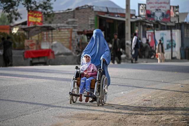 An Afghan burqa-clad woman pushes a girl on a wheelchair along a road in the Faizabad district of Badakhshan province on June 23, 2026. (Photo by Omer ABRAR / AFP)