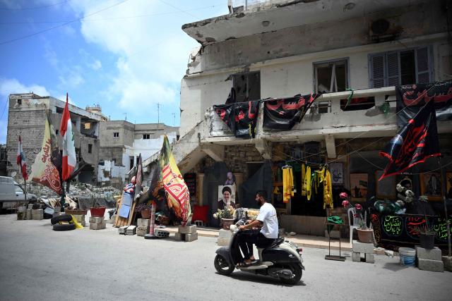 A man rides his motorbike past a damaged house decorated with Hezbollah party scarves and Shia Muslim Ashura flags as the Shia community marks the holy month of Ashura which commemorates the day one of Prophet Mohammed's grandsons was killed during a battle with unjustice King Yazid in 680 AD in Karbala of Iraq, in the southern Lebanese coastal city of Tyre on June 23, 2026. On June 22, 2026, mediators Pakistan and Qatar said that Tehran and Washington had agreed to set up a "de-confliction cell" to limit flare-ups in Lebanon following talks in Switzerland on ending the wider Middle East war, which Tehran has linked to halting the parallel conflict in Lebanon. (Photo by Joseph EID / AFP) / 