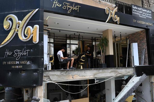 A hairdresser gives haircuts to his clients at his saloon damaged during previous the Israeli military strikes on the southern Lebanese coastal city of Tyre on June 23, 2026. On June 22, 2026, mediators Pakistan and Qatar said that Tehran and Washington had agreed to set up a "de-confliction cell" to limit flare-ups in Lebanon following talks in Switzerland on ending the wider Middle East war, which Tehran has linked to halting the parallel conflict in Lebanon. (Photo by Joseph EID / AFP) / 