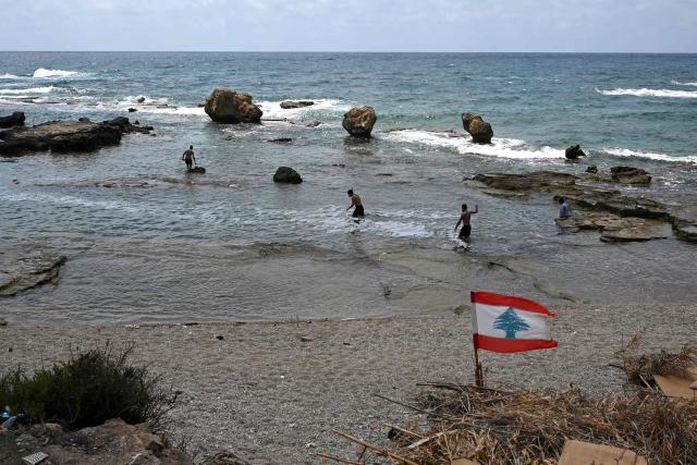 The Lebanese flag flutters as residents cool off in the Mediterranean Sea in the southern Lebanese coastal city of Tyre on June 23, 2026, days after the city saw numerous Israeli military strikes. On June 22, 2026, mediators Pakistan and Qatar said that Tehran and Washington had agreed to set up a "de-confliction cell" to limit flare-ups in Lebanon following talks in Switzerland on ending the wider Middle East war, which Tehran has linked to halting the parallel conflict in Lebanon. (Photo by Joseph EID / AFP) / 