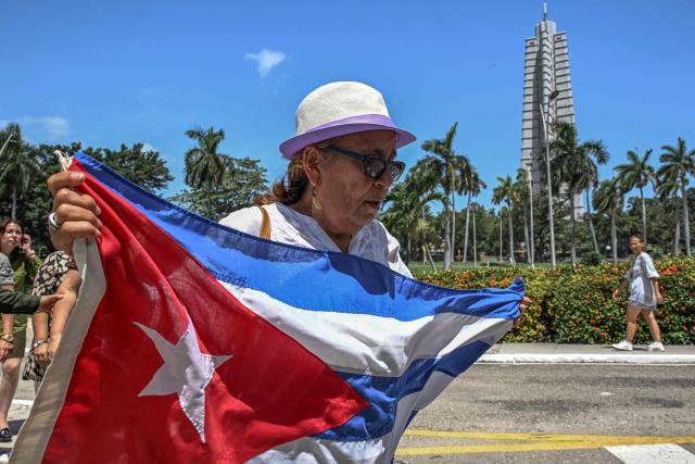 A woman holds a Cuban flag as she lines up in front of the Ministry of the Revolutionary Armed Forces to pay tribute to Commander Ramiro Valdés during his funeral in Havana on June 23, 2026. Ramiro Valdes Menendez, a close associate of brothers Fidel and Raul Castro and founder of the Cuban intelligence services, has died at the age of 94, Cuban President Miguel Diaz-Canel announced on June 21, 2026. (Photo by YAMIL LAGE / AFP)
