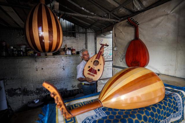 EDITORS NOTE: Graphic content / Displaced Palestinian craftsman Suhail Abu Shawish, who repairs musical instruments damaged by shelling or destruction during the war in the Gaza Strip using wooden pallets and leftover aid materials, prepares to hang up a "Ud" instrument at his makeshift shop in the Nuseirat camp for Palestinian refugees in the central Gaza Strip on June 23, 2026. (Photo by Eyad Baba / AFP)