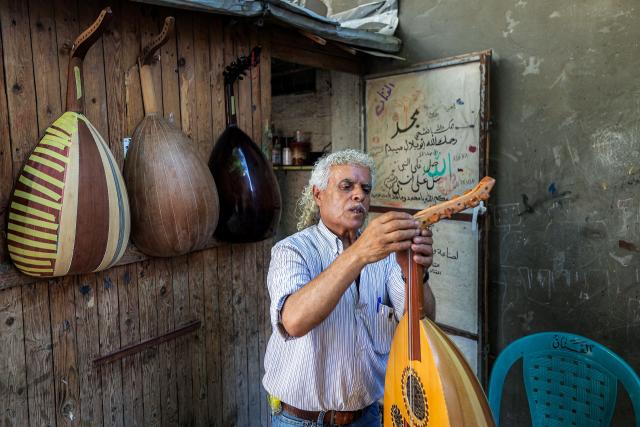EDITORS NOTE: Graphic content / Displaced Palestinian craftsman Suhail Abu Shawish tunes a "Ud" musical instrument he is repairing, damaged by shelling or destruction during the war in the Gaza Strip using wooden pallets and leftover aid materials, at his makeshift workshop in the Nuseirat camp for Palestinian refugees in the central Gaza Strip on June 23, 2026. (Photo by Eyad Baba / AFP)