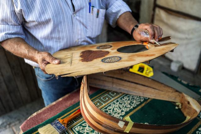 EDITORS NOTE: Graphic content / Displaced Palestinian craftsman Suhail Abu Shawish repairs a "Ud" musical instrument damaged by shelling or destruction during the war in the Gaza Strip using wooden pallets and leftover aid materials, at his makeshift workshop in the Nuseirat camp for Palestinian refugees in the central Gaza Strip on June 23, 2026. (Photo by Eyad Baba / AFP)