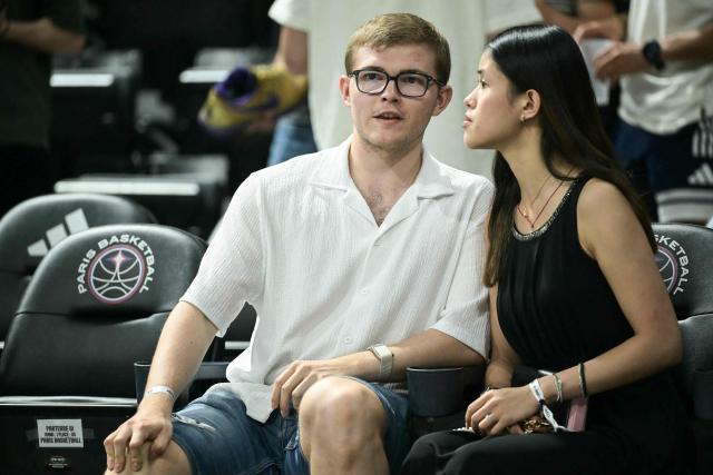 French table tennis player Alexis Lebrun (L) and his partner Melody Sok attend the French Ligue Nationale de Basket (LNB Elite) Pro A match 5 of the final between Paris Basketball and AS Monaco Basket, at the Adidas Arena in Paris on June 23, 2026. James is wearing the number 32, which is usually worn by his teammate Matthew Strazel, who is absent for this decisive match after being handed a one-match ban (plus a suspended one) on June 22, 2026 by the National Basketball League (LNB) disciplinary committee. (Photo by JULIEN DE ROSA / AFP)