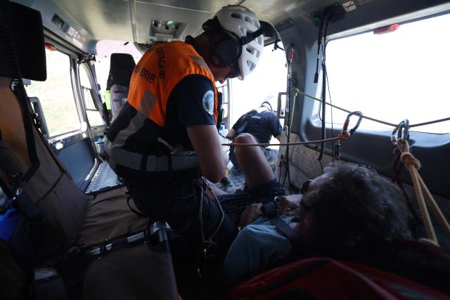 A member of Ajaccio's High Mountain Gendarmerie Platoon (PGHM, Peleton de Gendarmerie de Haute Montagne), an elite unit of the French Gendarmerie specialising in mountain rescue and law enforcement in high-altitude and alpine environments, cares about an injured man after winching him up into the gendarme helicopter to evacuate him to the hospital close from Ajaccio on the French Mediterranean island of Corsica on June 23, 2026. (Photo by Pascal POCHARD-CASABIANCA / AFP)