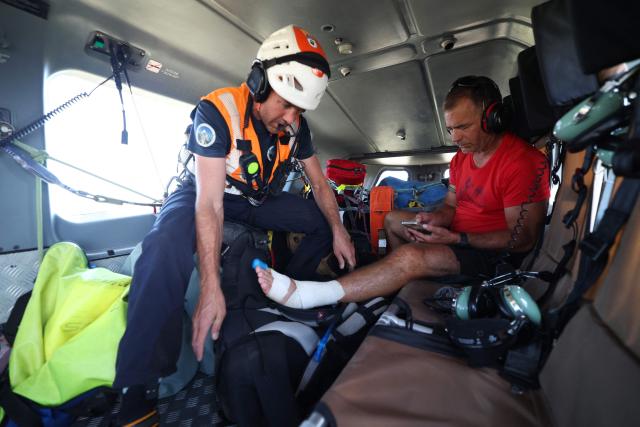 A member of Ajaccio's High Mountain Gendarmerie Platoon (PGHM, Peleton de Gendarmerie de Haute Montagne), an elite unit of the French Gendarmerie specialising in mountain rescue and law enforcement in high-altitude and alpine environments, evacuates an injured tourist on the GR20 hiking trail at the Asinau shelter in the Bavella mountain inside the gendarme helicopter in Zonza on the French Mediterranean island of Corsica on June 23, 2026. (Photo by Pascal POCHARD-CASABIANCA / AFP)