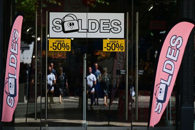 (FILES) People walk by a shop window of a store announcing discounts (Soldes in French) for the French summer sales, in Beziers, Southern France, on June 28, 2025. The summer sales kick off on June 24, 2026, amid scorching heat, "a godsend" for air-conditioned department stores where consumers take refuge, but a source of concern for downtown shops, which fear purchases will shift to ultra-fast-fashion online platforms. (Photo by GABRIEL BOUYS / AFP)