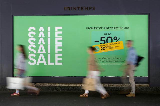(FILES) People walk past a board displayed on the shop window of a department store advertising discounts up to 50 % on the first day of the French summer sales in Paris on June 25, 2025. The summer sales kick off on June 24, 2026, amid scorching heat, "a godsend" for air-conditioned department stores where consumers take refuge, but a source of concern for downtown shops, which fear purchases will shift to ultra-fast-fashion online platforms. (Photo by Emma DA SILVA / AFP)