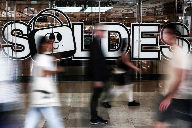 (FILES) People walk past the entrance door of a department store bearing a board announcing French summer sales on the first day in Paris on June 25, 2025. The summer sales kick off on June 24, 2026, amid scorching heat, "a godsend" for air-conditioned department stores where consumers take refuge, but a source of concern for downtown shops, which fear purchases will shift to ultra-fast-fashion online platforms. (Photo by Thibaud MORITZ / AFP)
