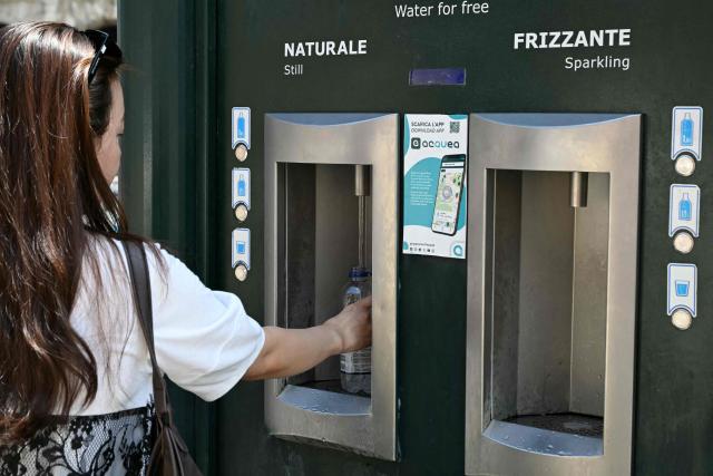 A tourist fills her bottle at a public fountain displaying still and sparkling refrigerated water for free, near the Colosseum on June 24, 2026. (Photo by Andreas SOLARO / AFP)