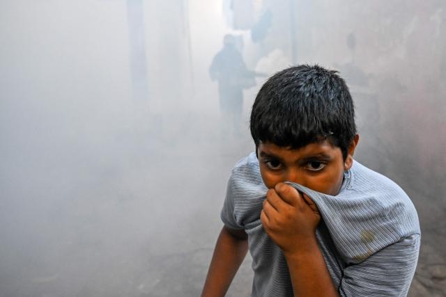 A boy covers his face as a municipal worker fumigates a residential area during a nationwide dengue prevention campaign in Colombo on June 24, 2026. (Photo by Ishara S. KODIKARA / AFP)