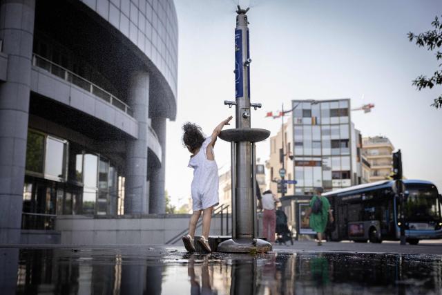 A child cools off at a public drinking fountain in Paris on June 24, 2026, as a heatwave hits France. (Photo by SIMON WOLFHART/STR / AFP)