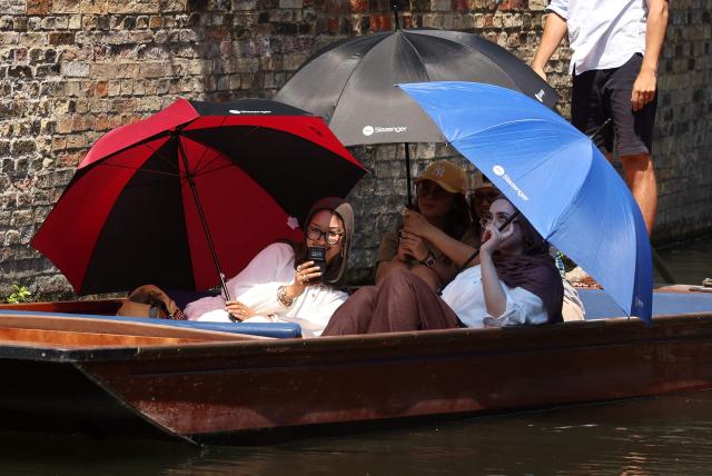 People shelter from the sun beneath umbrellas as they take a punt ride along the River Cam, during a heatwave, in Cambridge on June 24, 2026. The UK's meteorological office has issued an extremely rare red heat warning -- only issued once before -- for June24 and 25, as temperatures could soar to 40C, unprecedented for the time of the year. (Photo by Chris RADBURN / AFP)