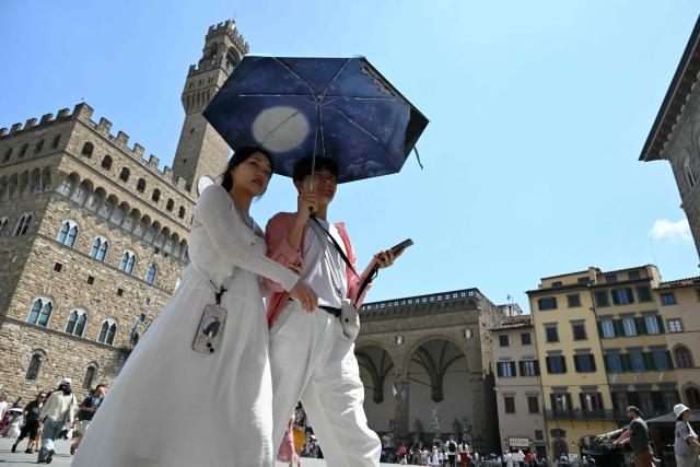 TOPSHOT - A couple shields themselves from the sun under an umbrella as they walk through Piazza della Signoria in Florence during a heatwave on June 24, 2026. (Photo by Alberto PIZZOLI / AFP)