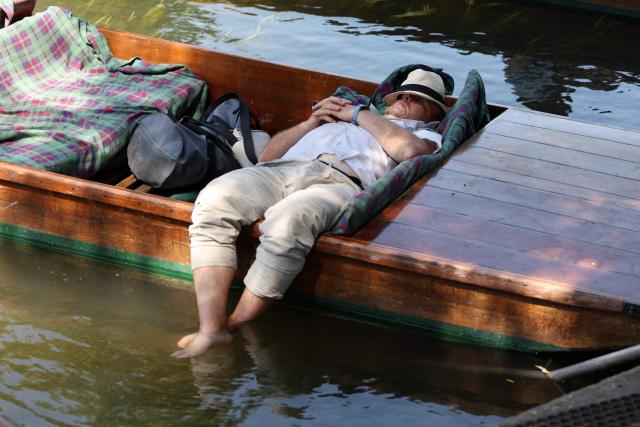 A punt chauffer relaxes with their feet in the water between punt tours on the River Cam, during a heatwave, in Cambridge on June 24, 2026. The UK's meteorological office has issued an extremely rare red heat warning -- only issued once before -- for June24 and 25, as temperatures could soar to 40C, unprecedented for the time of the year. (Photo by Chris RADBURN / AFP)