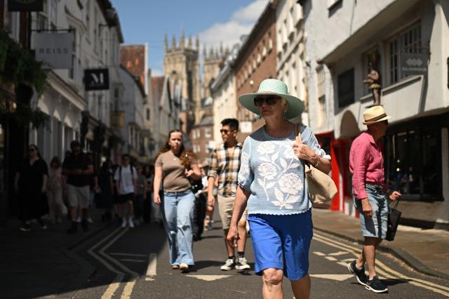 People walk in the sun past shops during a heatwave, in York, on June 24, 2026. The UK's meteorological office has issued an extremely rare red heat warning -- only issued once before -- for June24 and 25, as temperatures could soar to 40C, unprecedented for the time of the year. (Photo by Oli SCARFF / AFP)