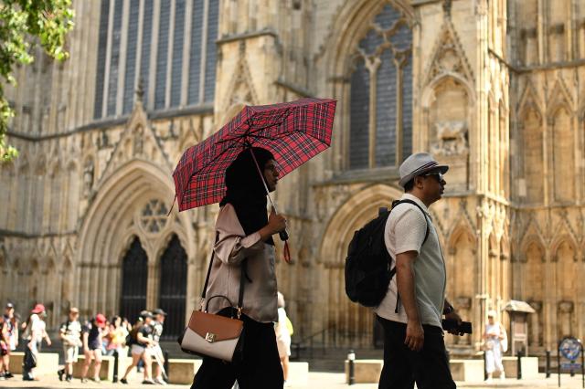 A person shelters from the sun as they walk past York Minster during a heatwave, in York, on June 24, 2026. The UK's meteorological office has issued an extremely rare red heat warning -- only issued once before -- for June24 and 25, as temperatures could soar to 40C, unprecedented for the time of the year. (Photo by Oli SCARFF / AFP)