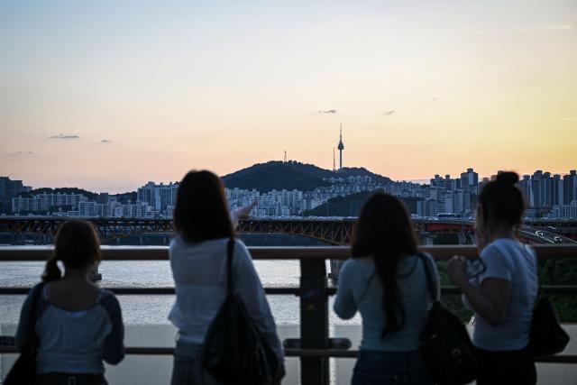 People look on from a bridge over the Hangang River as the Seoul Tower is seen in the background in Seoul on June 24, 2026. (Photo by Jade Gao / AFP)
