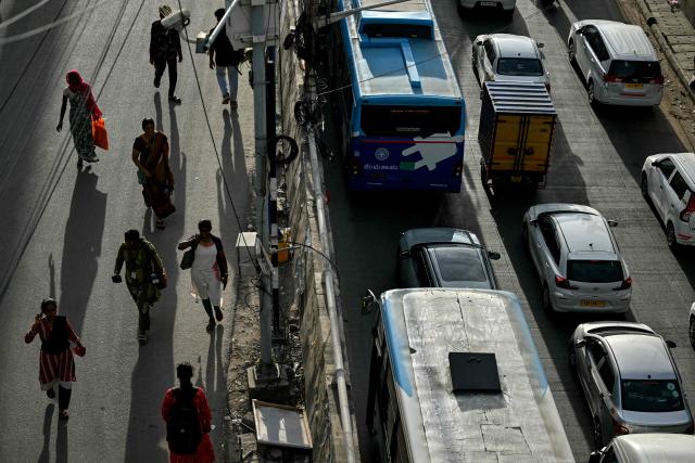 Pedestrians walk along a road as vehicles move through traffic in Bengaluru on June 24, 2026. (Photo by Idrees MOHAMMED / AFP)