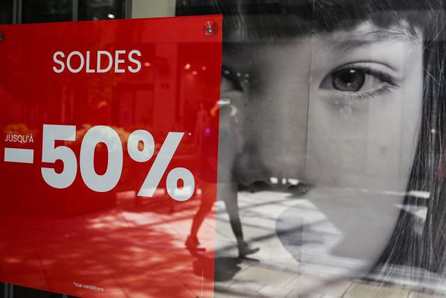 Pedestrians walk past the entrance of a department store bearing a placard promoting French summer sales on the opening day in Beziers, Southern France, on June 24, 2026. The summer sales kick off on June 24, 2026, amid scorching heat, "a godsend" for air-conditioned department stores where consumers take refuge, but a source of concern for downtown shops, which fear purchases will shift to ultra-fast-fashion online platforms. (Photo by Gabriel BOUYS / AFP)
