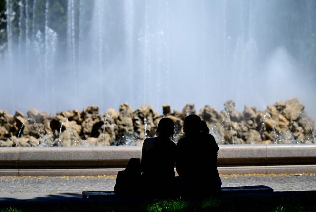 People silhouette against the spray mist of a fountain on June 24, 2026 in Vienna, Austria, where temperatures reached more than 30 degrees Celsius. (Photo by ROLAND SCHLAGER / APA / AFP) / Austria OUT