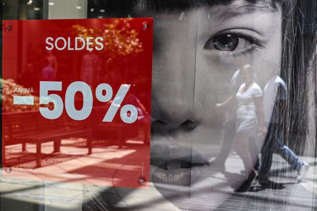 Pedestrians walk past the entrance of a department store bearing a placard promoting French summer sales on the opening day in Beziers, Southern France, on June 24, 2026. The summer sales kick off on June 24, 2026, amid scorching heat, "a godsend" for air-conditioned department stores where consumers take refuge, but a source of concern for downtown shops, which fear purchases will shift to ultra-fast-fashion online platforms. (Photo by Gabriel BOUYS / AFP)