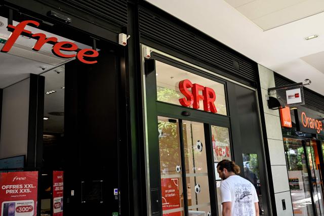 A pedestrian walks by shop windows of Free telecom, SFR telecom and Orange Telecom in Beziers, Southern France, on June 24, 2026. Three of France's mobile operators (Bouygues Telecom, Free and Orange) have agreed a joint bid worth 20.4 billion euros ($23.5 billion) for rival SFR, owned by indebted French-Luxembourg telco group Altice. (Photo by Gabriel BOUYS / AFP)