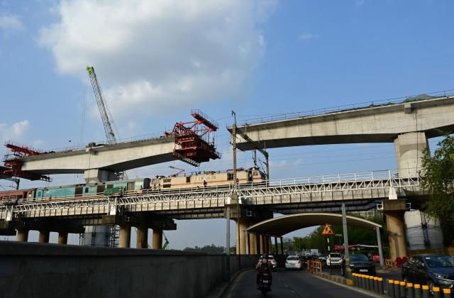 A passenger train rides past an under-construction section of the Ahmedabad-Mumbai high-speed rail project at the Sabarmati riverfront in Ahmedabad on June 24, 2026. (Photo by Shammi MEHRA / AFP)
