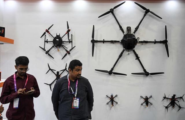 Exibitors stand beside drones displayed at the International Police and Drone Expo 2026 in New Delhi on June 24, 2026. (Photo by Arun SANKAR / AFP)
