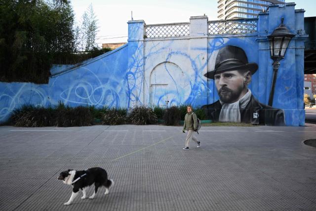 A woman walks her dog near a mural depicting Argentine football star Lionel Messi in Buenos Aires on June 24, 2026, during the FIFA World Cup 2026. (Photo by Luis ROBAYO / AFP)