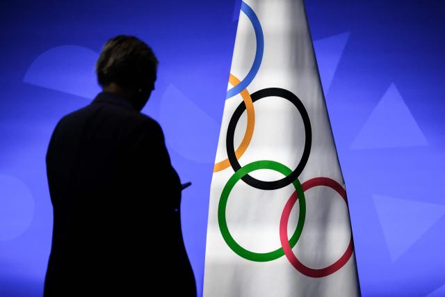 A staff of the International Olympic Committee President (IOC) is silhouetted next to an Olympic flag during a IOC session, in Lausanne, on June 24, 2026. (Photo by Fabrice COFFRINI / AFP)