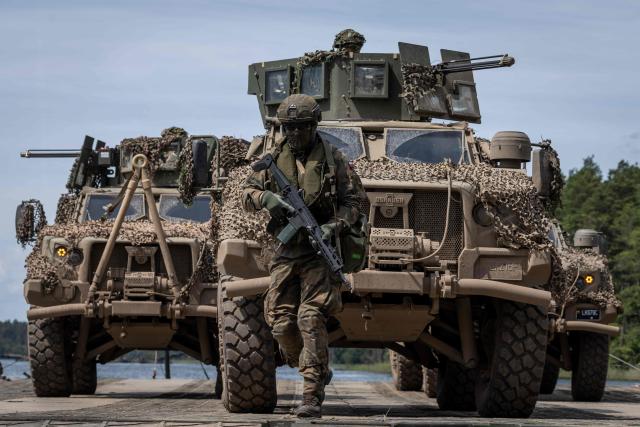 A Polish soldier is seen in front of two Lithuanian Armed Forces US-made Oshkosh JLTV (Joint Light Tactical Vehicle), on the deck of a Polish Army PFM Motorised Floating Bridge during a lake crossing as troops from Poland and Lithuania take part in the "Bursztynowy Obronca-26" (Amber Defender) military exercise on the Orzysz military training ground, north-eastern Poland, on June 24, 2026. (Photo by Wojtek RADWANSKI / AFP)