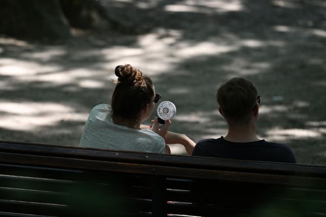 A woman uses a portable fan to cool off as she sits on bench in the Parc du Cinquantenaire during a heatwave, in Brussels on June 24, 2026. (Photo by Nicolas TUCAT / AFP)