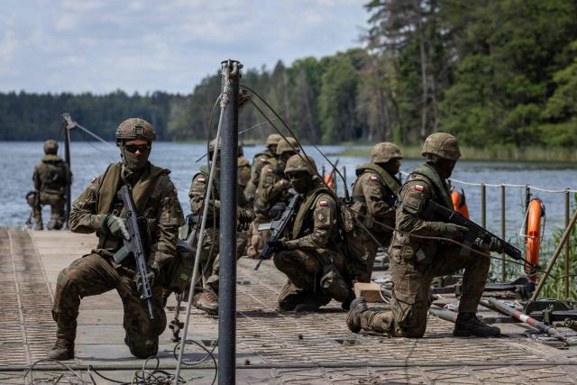 Polish soldiers kneel on the deck of a Polish Army PFM Motorised Floating Bridge during a lake crossing, as troops from Poland and Lithuania take part in the "Bursztynowy Obronca-26" (Amber Defender) military exercise on the Orzysz military training ground, north-eastern Poland, on June 24, 2026. (Photo by Wojtek RADWANSKI / AFP)