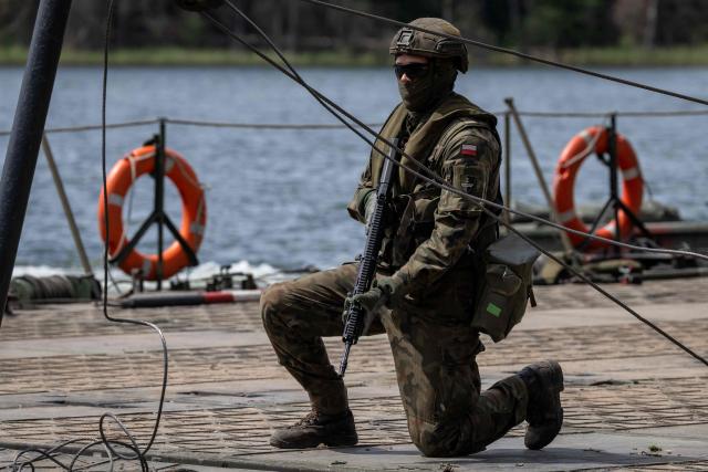 A Polish soldier kneels on the deck of a Polish Army PFM Motorised Floating Bridge during a lake crossing, as troops from Poland and Lithuania take part in the "Bursztynowy Obronca-26" (Amber Defender) military exercise on the Orzysz military training ground, north-eastern Poland, on June 24, 2026. (Photo by Wojtek RADWANSKI / AFP)