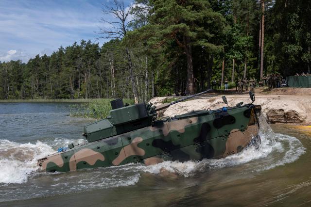 A Polish-made Borsuk amphibious Infantry Fighting Vehicle (IFV) drives onto the shore after crossing a lake, as troops from Poland and Lithuania take part in the "Bursztynowy Obronca-26" (Amber Defender) military exercise on the Orzysz military training ground, north-eastern Poland, on June 24, 2026. (Photo by Wojtek RADWANSKI / AFP)