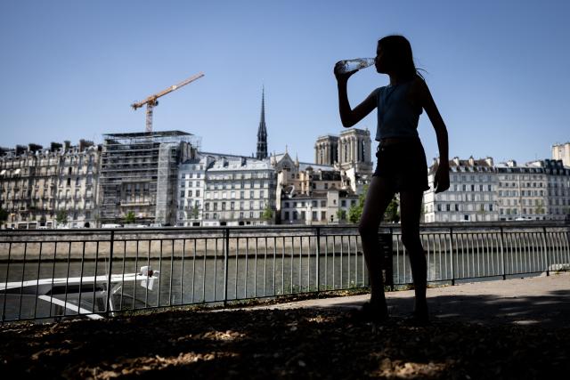 (FILES) A pedestrian drinks water from a plastic bottle as she walks along the Georges Pompidou expressway in Paris on June 24, 2026. France experienced its hottest day ever recorded on June 24, 2026, surpassing the record set the previous day, according to national weather service Meteo-France. (Photo by Simon WOHLFAHRT / AFP)
