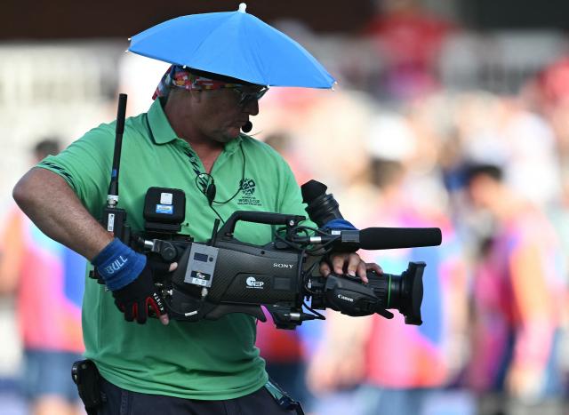 A television camera operator wears a parasol umbrella on their head as players walk out for the ICC Women's T20 cricket world cup 2026 match between England and West Indies, at Lord's in London on June 24, 2026. (Photo by JUSTIN TALLIS / AFP)