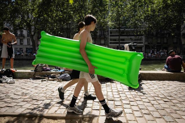 a youth carries an inflatable pool float next to the Canal Saint-Martin during a heatwave in Paris in Paris on June 24, 2026. France experienced its hottest day ever recorded on June 24, 2026, surpassing the record set the previous day, according to national weather service Meteo-France. (Photo by Simon WOHLFAHRT / AFP)