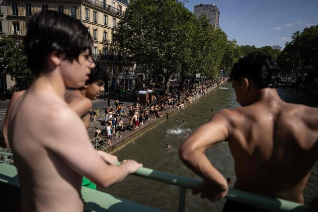 Youths observe from a bridge before jumping into the Canal Saint-Martin during a heatwave in Paris in Paris on June 24, 2026. France experienced its hottest day ever recorded on June 24, 2026, surpassing the record set the previous day, according to national weather service Meteo-France. (Photo by Simon WOHLFAHRT / AFP)