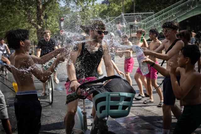 A group of teenagers throw water at a cyclist next to the Canal Saint-Martin during a heatwave, in Paris on June 24, 2026. France experienced its hottest day ever recorded on June 24, 2026, surpassing the record set the previous day, according to national weather service Meteo-France. (Photo by Simon WOHLFAHRT / AFP)